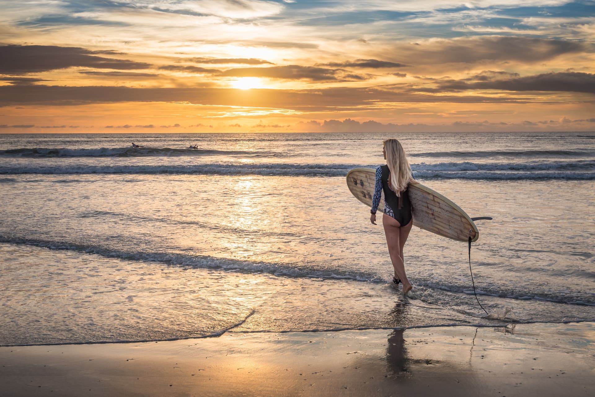 Surfer walking into the ocean at sunset carrying a surfboard, golden light reflecting on the water